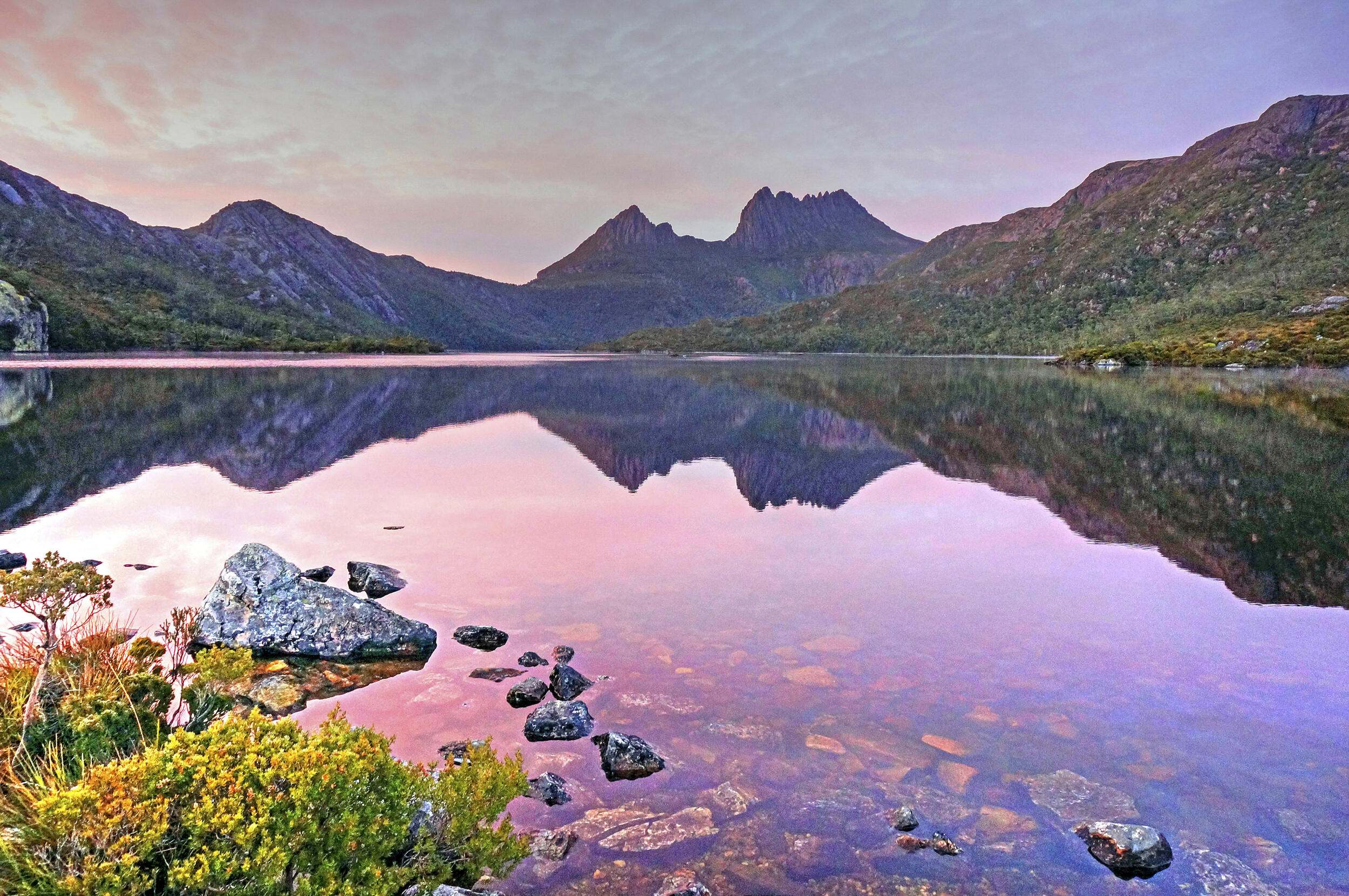 A view over a lake showing pink from the dawn, surrounded by mountains